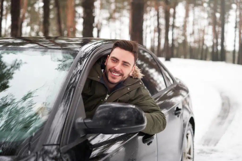 Young man driving through the snow in new car - Tom's Auto Tag